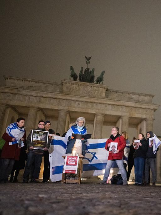 Menschen stehen im Morgengrauen am Brandenburger Tor und lesen die Namen der Opfer vom 7. Oktober 2023 vor. Einige von ihnen tragen Israelfahnen Menschen stehen im Morgengrauen am Brandenburger Tor und lesen die Namen der Opfer vom 7. Oktober 2023 vor. Einige von ihnen tragen Israelfahnen