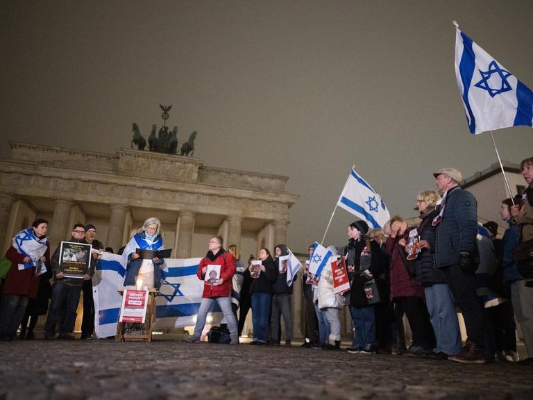 Menschen stehen im Morgengrauen am Brandenburger Tor und lesen die Namen der Opfer vom 7. Oktober 2023 vor. Einige von ihnen tragen Israelfahnen Menschen stehen im Morgengrauen am Brandenburger Tor und lesen die Namen der Opfer vom 7. Oktober 2023 vor. Einige von ihnen tragen Israelfahnen