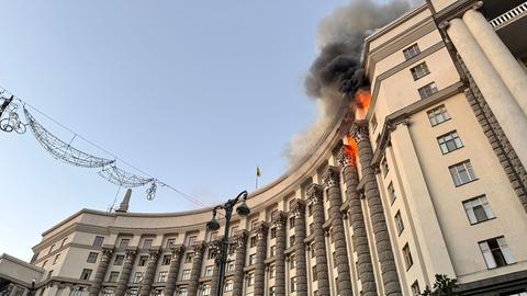 Blick von unten auf die Fassade des großen Gebäudes der ukrainischen Regierung, in der obersten Etage schlagen Flammen aus mehreren Fenstern.