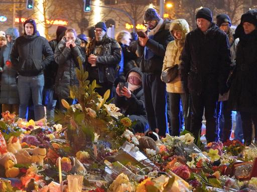 Menschen stehen vor einem Meer aus Blumen und gedenken der Toten des Magdeburger Terranschlags