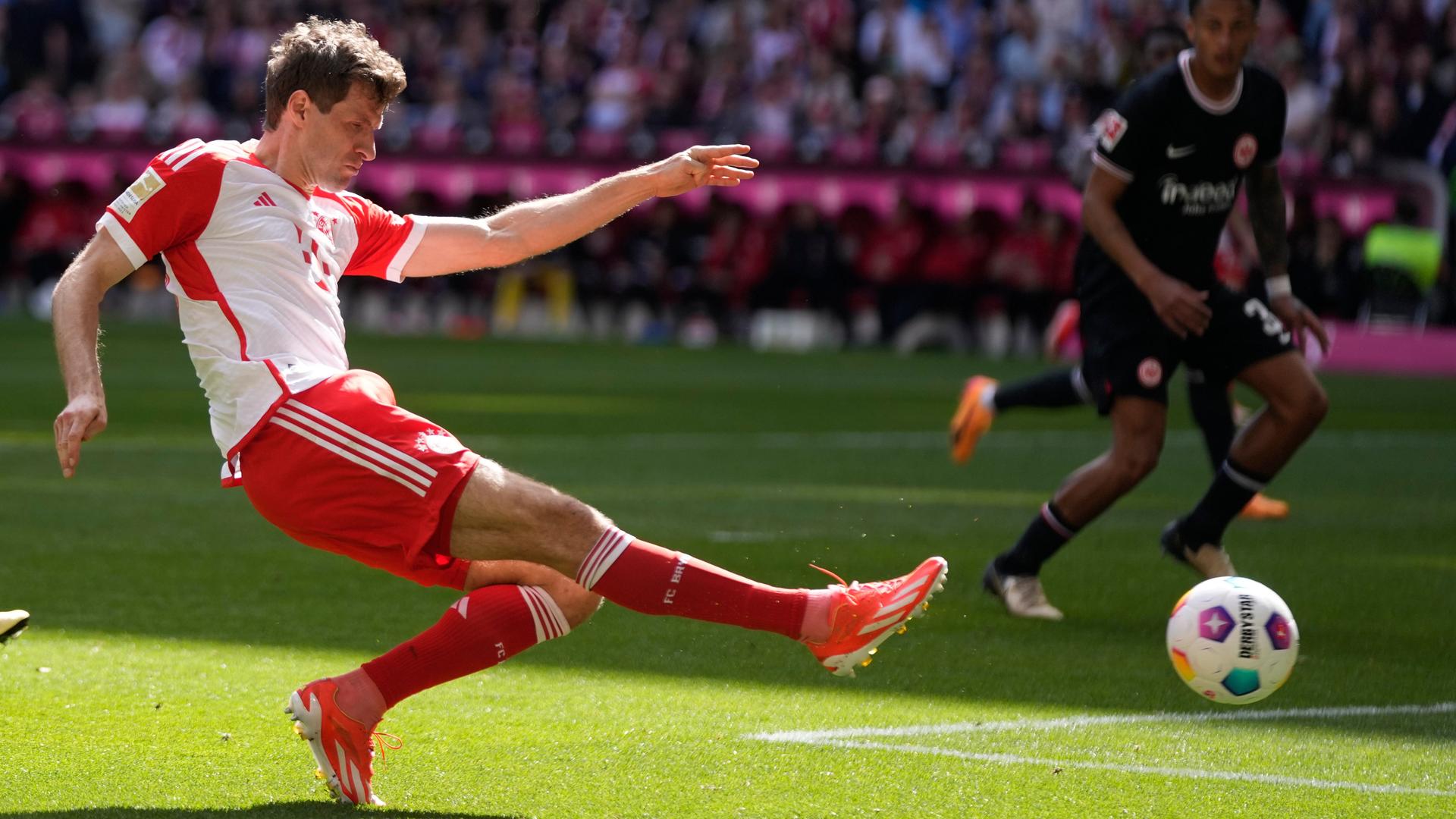 Müller schießt den Ball mit ausgestrecktem Bein, dahinter zwei Frankfurter Gegenspieler.