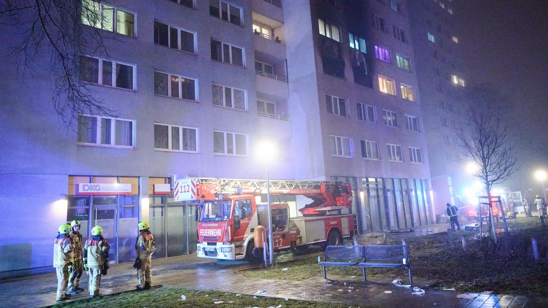 Feuerwehrleute stehen für Löscharbeiten vor einem Wohnhaus. Auch ein Feuerwehrwagen steht dort.