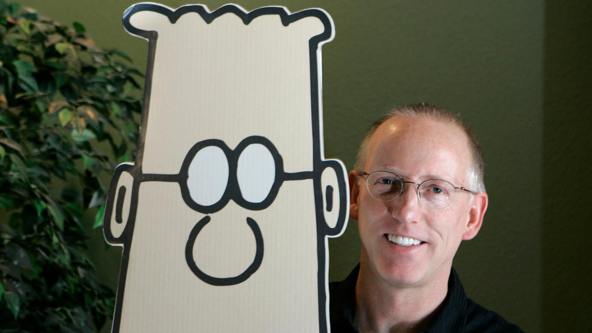 Der Cartoonist Scott Adams legt beide Hände auf die Schultern seiner Papp-Comicfigur Dilbert.
