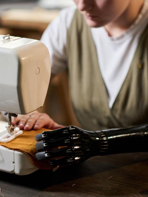 Eine junge Frau mit einer Unterarmprothese arbeitet an einer Nähmaschine. (Symbolbild)