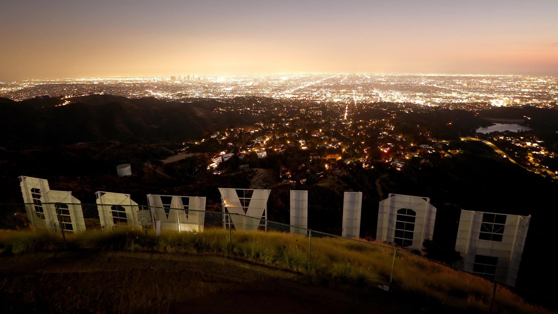 Der ikonische Hollywood-Schriftzug in der Abenddämmerung in der Rückansicht fotografiert mit Blick auf die Lichter von Los Angeles.