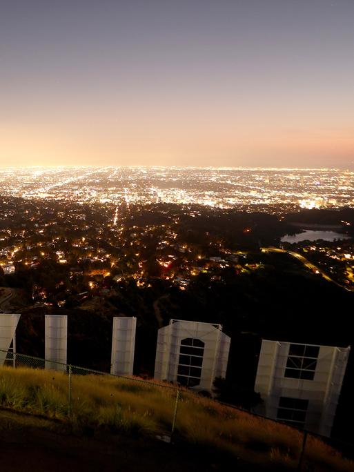 Der ikonische Hollywood-Schriftzug in der Abenddämmerung in der Rückansicht fotografiert mit Blick auf die Lichter von Los Angeles.