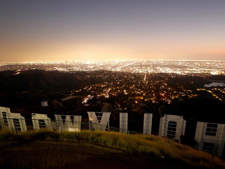 Der ikonische Hollywood-Schriftzug in der Abenddämmerung in der Rückansicht fotografiert mit Blick auf die Lichter von Los Angeles.