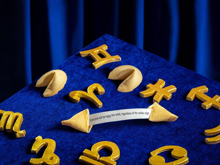 Sternzeichensymbole und Gleckskekse sind auf einem samtig blauen Hintergrund arrangiert.