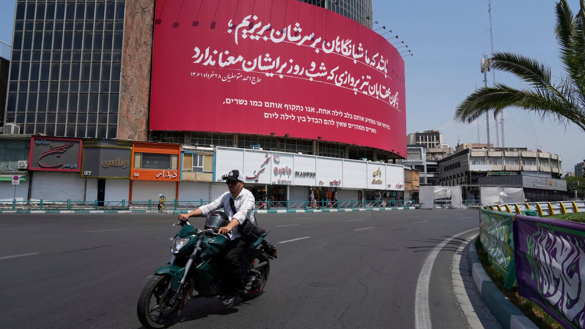 Ein Mann fährt mit seinem Motorrad an einem anti-israelischen Transparent vorbei auf dem Vali-e-Asr-Platz in Teheran, Iran.