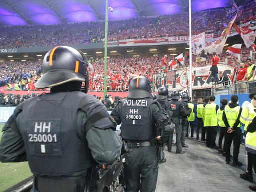 Polizisten stehen in einem Fußball--Stadion. Sie beobachten die Fans.