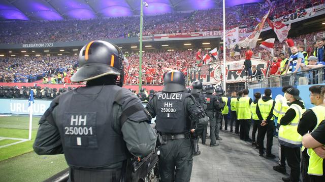 Polizisten stehen in einem Fußball--Stadion. Sie beobachten die Fans.