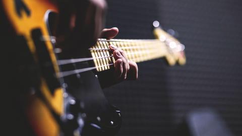 Stimmungsvolles Bild von einer Person, die Bassgitarre spielt. Von der Person sieht man nur die Hände an den Saiten.