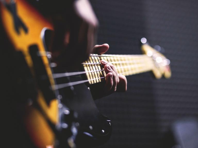 Stimmungsvolles Bild von einer Person, die Bassgitarre spielt. Von der Person sieht man nur die Hände an den Saiten.
