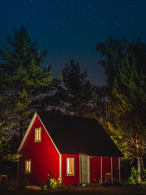 Ein kleines rotes Haus bei Nacht in einem Wald.