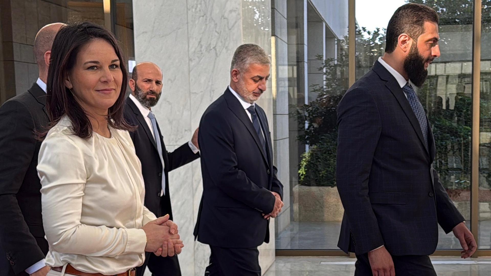 Außenministerin Annalena Baerbock (l) lächelt und geht hinter dem neuen syrischen Machthaber Ahmed al-Scharaa (r) durch den Präsidentenpalast in Damaskus.