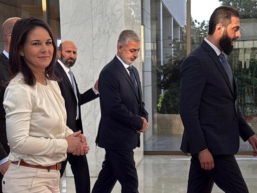 Außenministerin Annalena Baerbock (l) lächelt und geht hinter dem neuen syrischen Machthaber Ahmed al-Scharaa (r) durch den Präsidentenpalast in Damaskus.