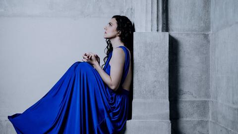 Die Pianistin sitzt in einem tiefblauem Kleid auf einem Gebäudevorsprung mit Säule, der an eine griechische Tempelanlage erinnert.