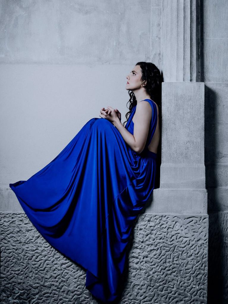 Die Pianistin sitzt in einem tiefblauem Kleid auf einem Gebäudevorsprung mit Säule, der an eine griechische Tempelanlage erinnert.