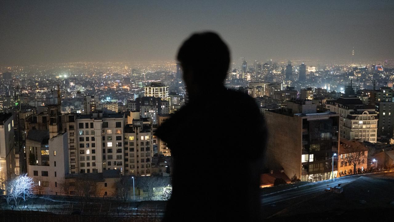 Ein Mann ist von hinten zu sehen und blickt nach Sonnenuntergang auf die Millionenmetropole Teheran.