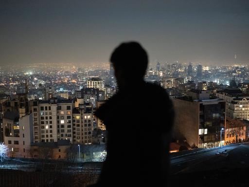 Ein Mann ist von hinten zu sehen und blickt nach Sonnenuntergang auf die Millionenmetropole Teheran.