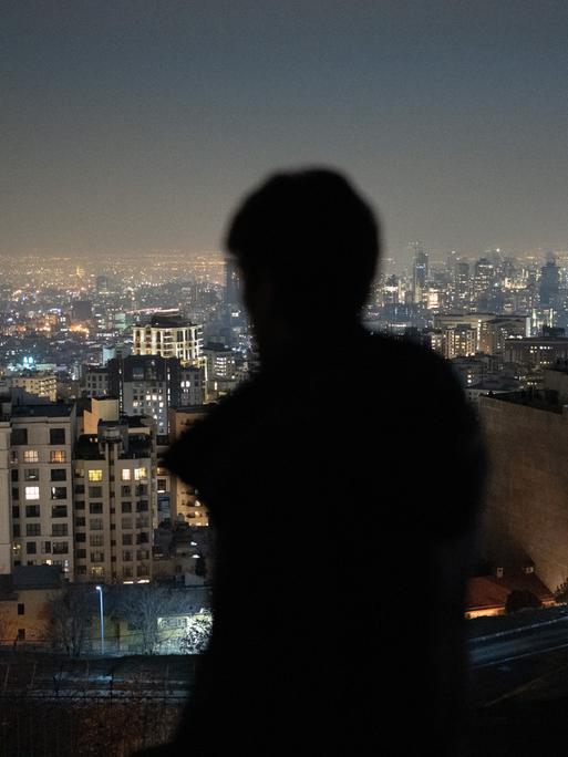 Ein Mann ist von hinten zu sehen und blickt nach Sonnenuntergang auf die Millionenmetropole Teheran.