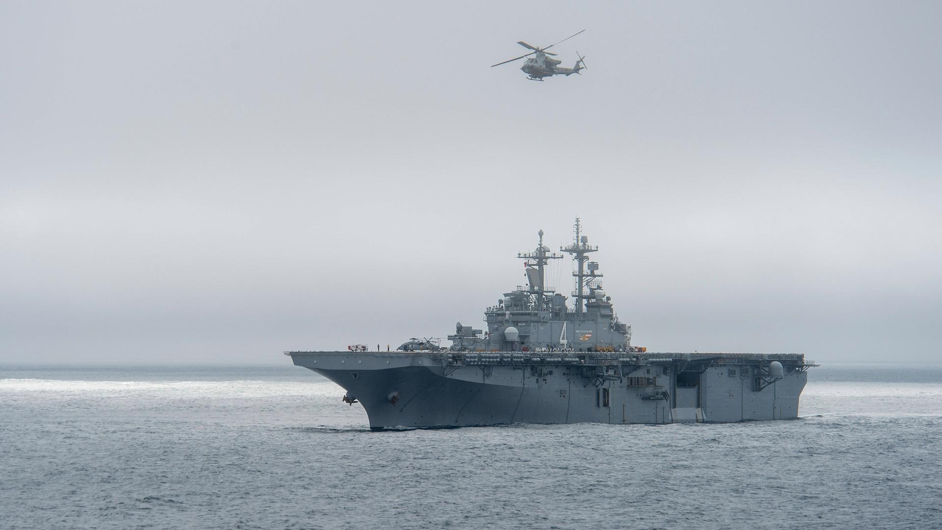 Auch das Angriffsschiff "USS Boxer" auf dem Meer, darüber fliegt ein Helikopter.
