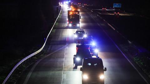 In der Nacht fährt ein Schwerlast-Transporter über eine Autobahn, begleitet von Polizeifahrzeugen.