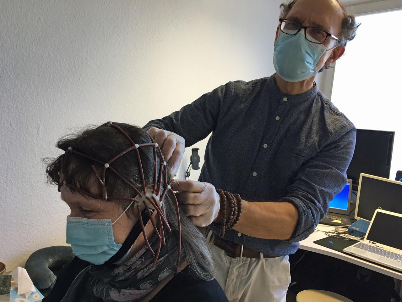 Mira Bussewitz bekommt Elektroden an den Kopf gelegt zur Messung der Hirnströme, im Hintergrund ist Christoph Ziaja zu sehen.