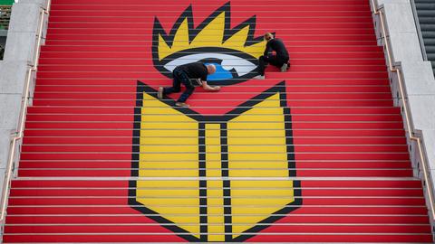 Eine Werbetechnikerin und ein Werbetechniker kleben das Logo der Leipziger Buchmesse auf eine Treppe in der Glashalle der Leipziger Messe.