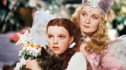 In dem Szenenbild von "Der Zauberer von Oz" schaut Judy Garland in der Rolle der "Dorothy" gebannt nach vorn, hinter ihr steht Billie Burke als 'Glinda'.