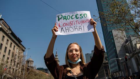 Eine junge Frau trägt während eines Protests ein Schild, das eine neue Verfassung fordert.