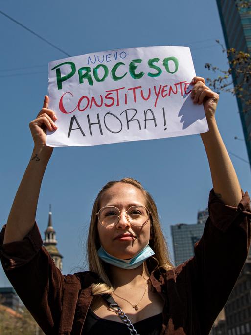 Eine junge Frau trägt während eines Protests ein Schild, das eine neue Verfassung fordert.