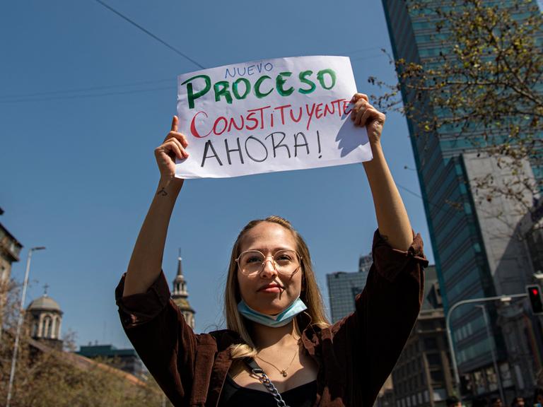 Eine junge Frau trägt während eines Protests ein Schild, das eine neue Verfassung fordert.