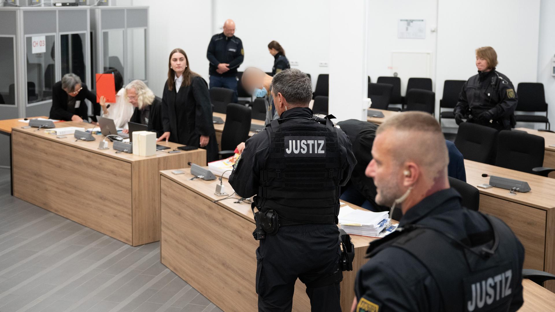 Dresden: Der Hauptangeklagte Jian G. (M) und eine Mitangeklagte (2.v.l., von einem roten Ordner verdeckt) stehen und sitzen zu Prozessbeginn im den Gerichtssaal. Dresden: Der Hauptangeklagte Jian G. (M) und eine Mitangeklagte (2.v.l., von einem roten Ordner verdeckt) stehen und sitzen zu Prozessbeginn im den Gerichtssaal.