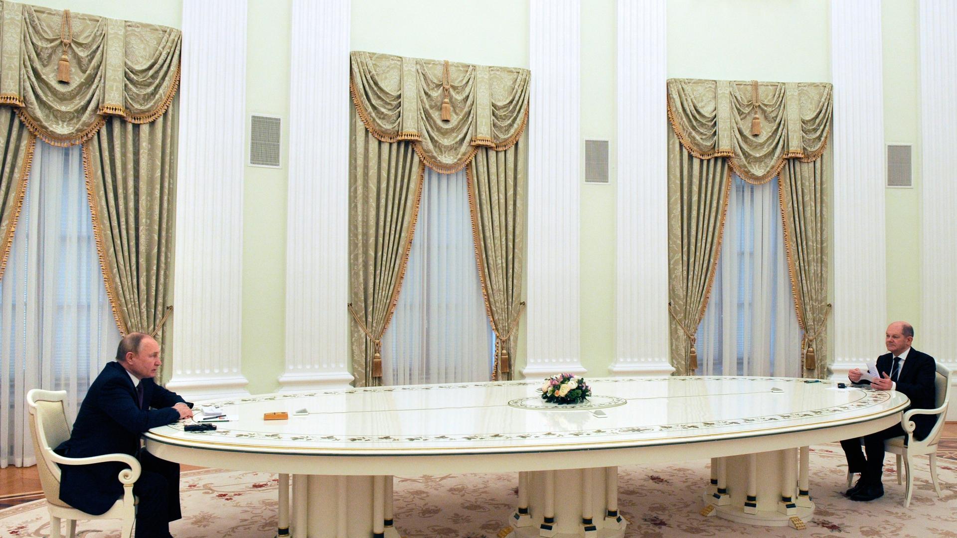 Der russische Präsident Wladimir Putin sitzt mit Bundeskanzler Olaf Scholz an einem großen weißen Tisch
