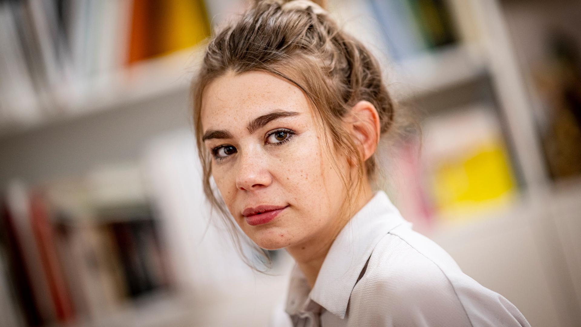 Porträt der Schriftstellerin und Moderatorin Ronja von Rönne, sie sitzt in ihrer Wohnung vor einer Bücherwand. Porträt der Schriftstellerin und Moderatorin Ronja von Rönne, sie sitzt in ihrer Wohnung vor einer Bücherwand.