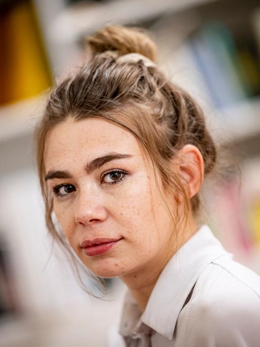 Porträt der Schriftstellerin und Moderatorin Ronja von Rönne, sie sitzt in ihrer Wohnung vor einer Bücherwand. 