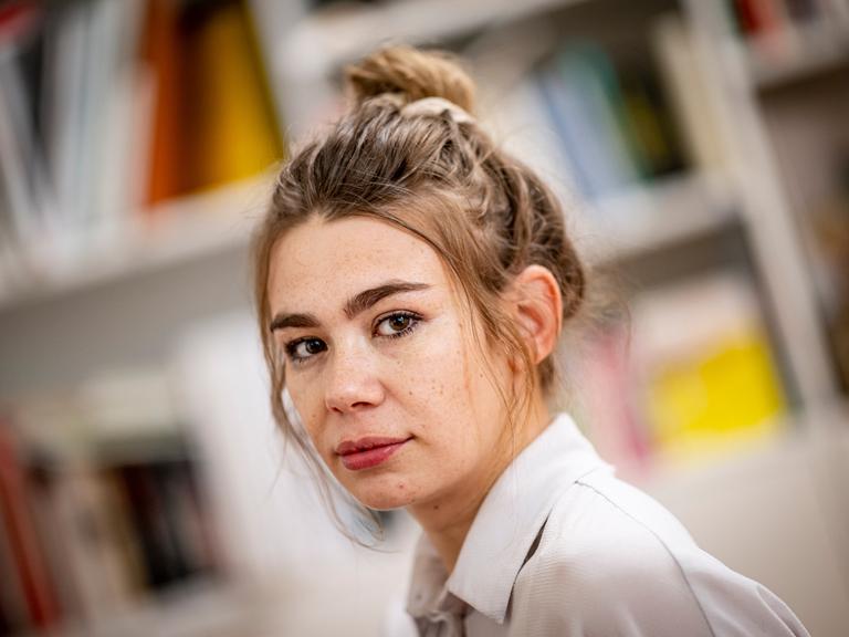 Porträt der Schriftstellerin und Moderatorin Ronja von Rönne, sie sitzt in ihrer Wohnung vor einer Bücherwand. 