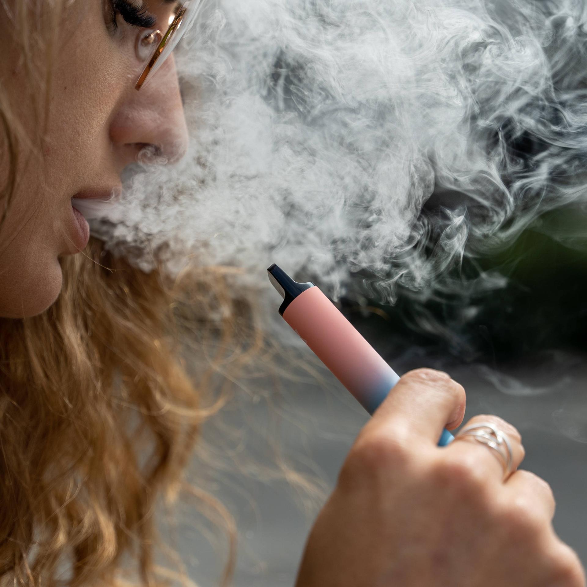Eine Frau raucht eine E-Zigarette, es qualmt stark.