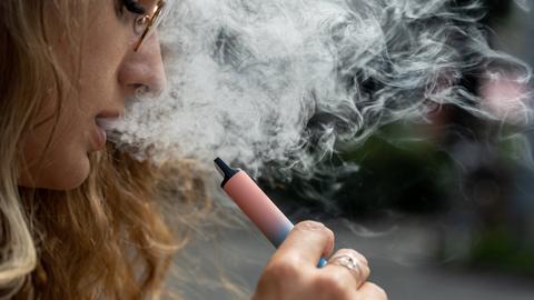 Eine Frau raucht eine E-Zigarette, es qualmt stark.
