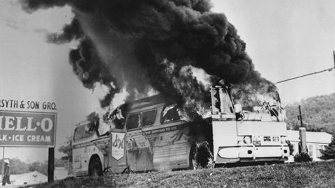 Ein Schwarz-Weiß-Foto zeigt einen der Busse des "Freedom Rides", der bei Anniston in Flammen steht. Es steigt dunkler Rauch auf.
