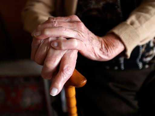 Nahaufnahme der Hände einer Seniorin, die sich an einem Gehstock festhält.