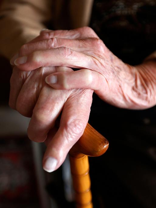 Nahaufnahme der Hände einer Seniorin, die sich an einem Gehstock festhält.