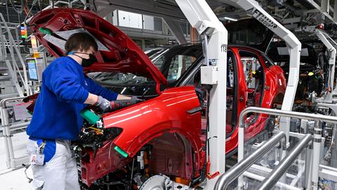 Ein Handwerker im Overall arbeitet in der Fertigungsstraße an einem roten E-Auto unter der Motorhaube (Symbolbild)