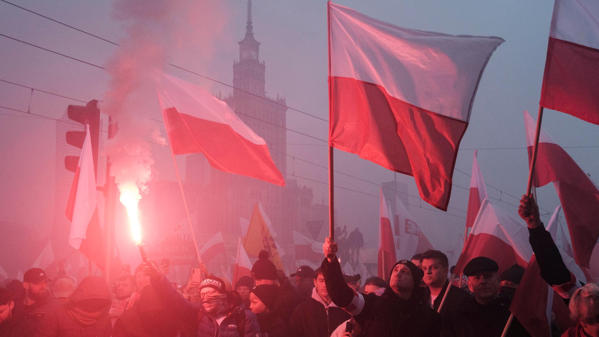 An einem nebligen Tag schwenken Protestierende polnische Flaggen. Im Hintergrund ist die Silhouette des Warschauer Kulturpalastes zu sehen. An einem nebligen Tag schwenken Protestierende polnische Flaggen. Im Hintergrund ist die Silhouette des Warschauer Kulturpalastes zu sehen.