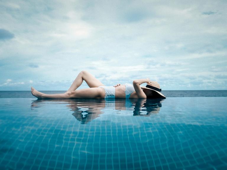 Eine Frau liegt im Bikini am Rand eines Pools, im Hintergrund das Meer.