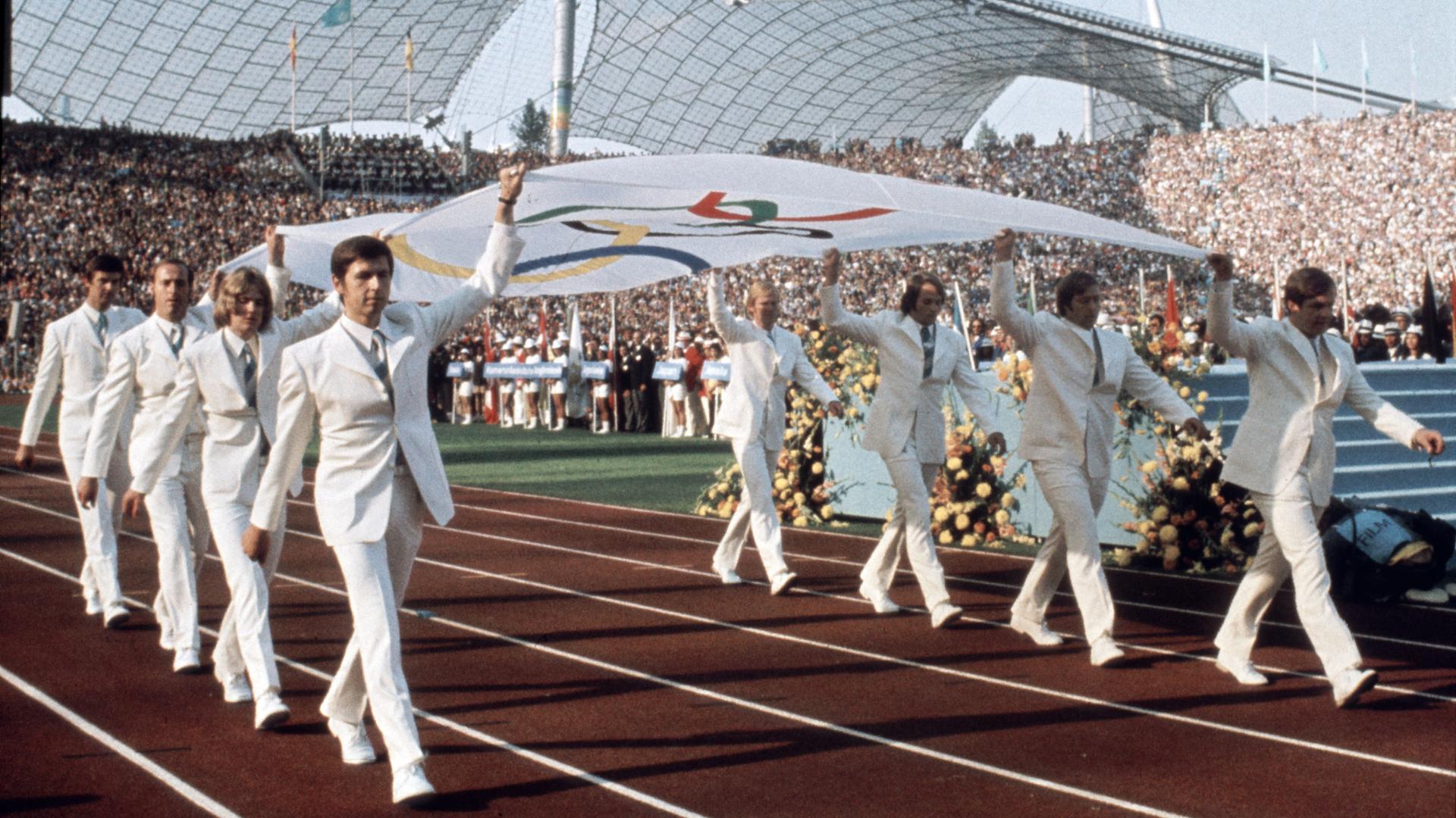 Die Mannschaft des deutschen Gold-Achter (Rudern) von Mexiko 1968 trägt die Olympische Fahne feierlich ins Stadion: (l-r): Egbert Hirschfelder, Rüdiger Henning, Steuermann Gunther Tiersch, Schlagmann Horst Meyer, Jörg Siebert, Roland Böse, Niko Ott und Dirk Schreyer. Blick in das Münchener Olympiastadion während der Eröffnungsfeier der Olympischen Sommerspiele am 26. August 1972.