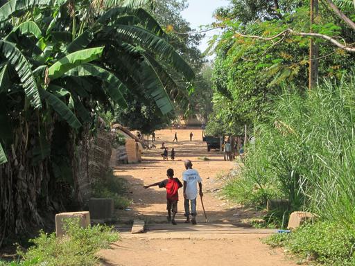 Zwei Kinder gehen eine Straße in der zentralafrikanischen Stadt Ndélé entlang. Sie sind von hinten und in größerer Entfernung zu sehen. 