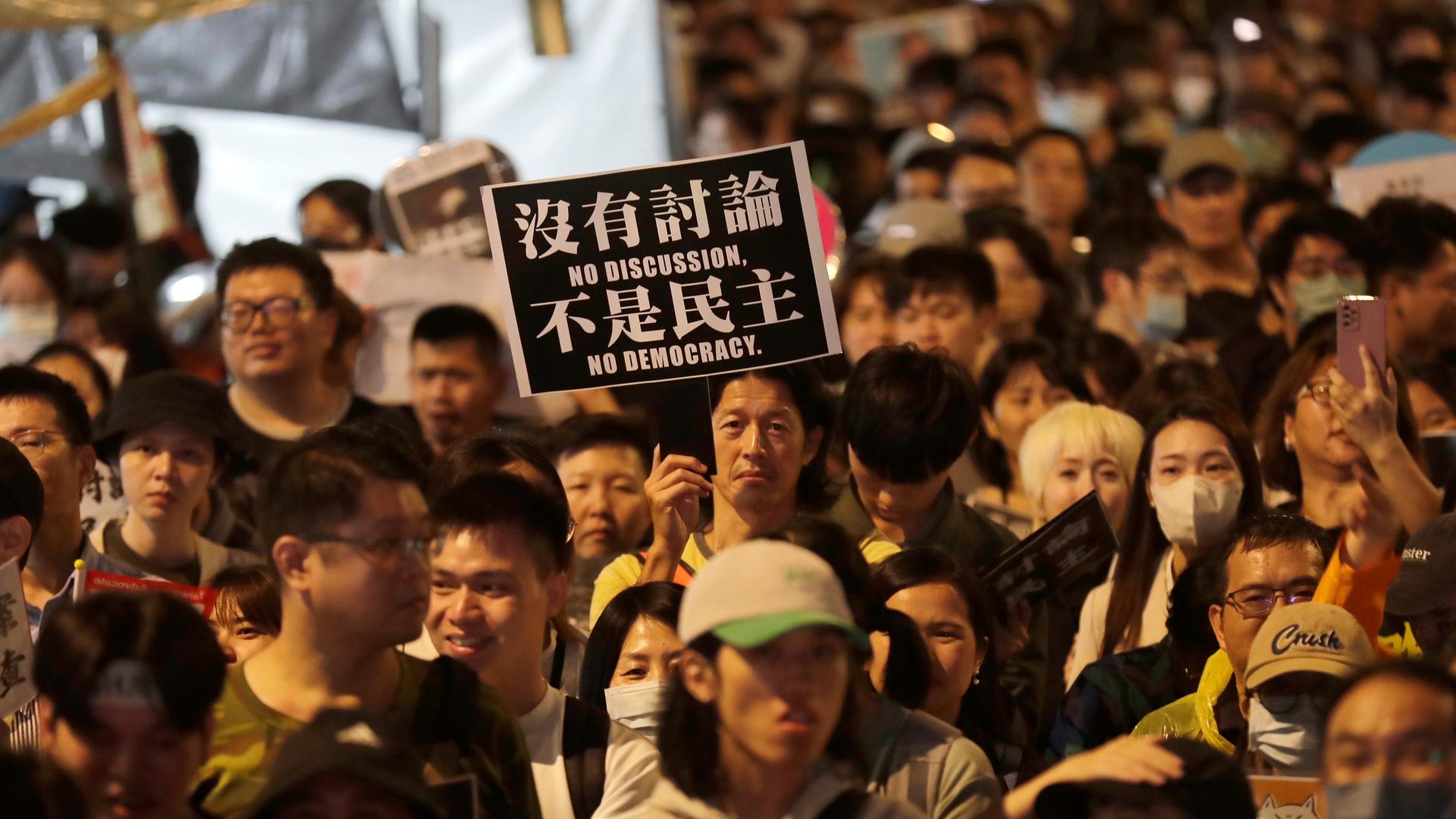 Anhänger der Demokratischen Fortschritspartei protestieren vor Parlament in Taiwan. Ein Demonstrant hält ein Schild mit der Aufschrift "Keine Diskussion - Keine Demokratie" in die Höhe. 