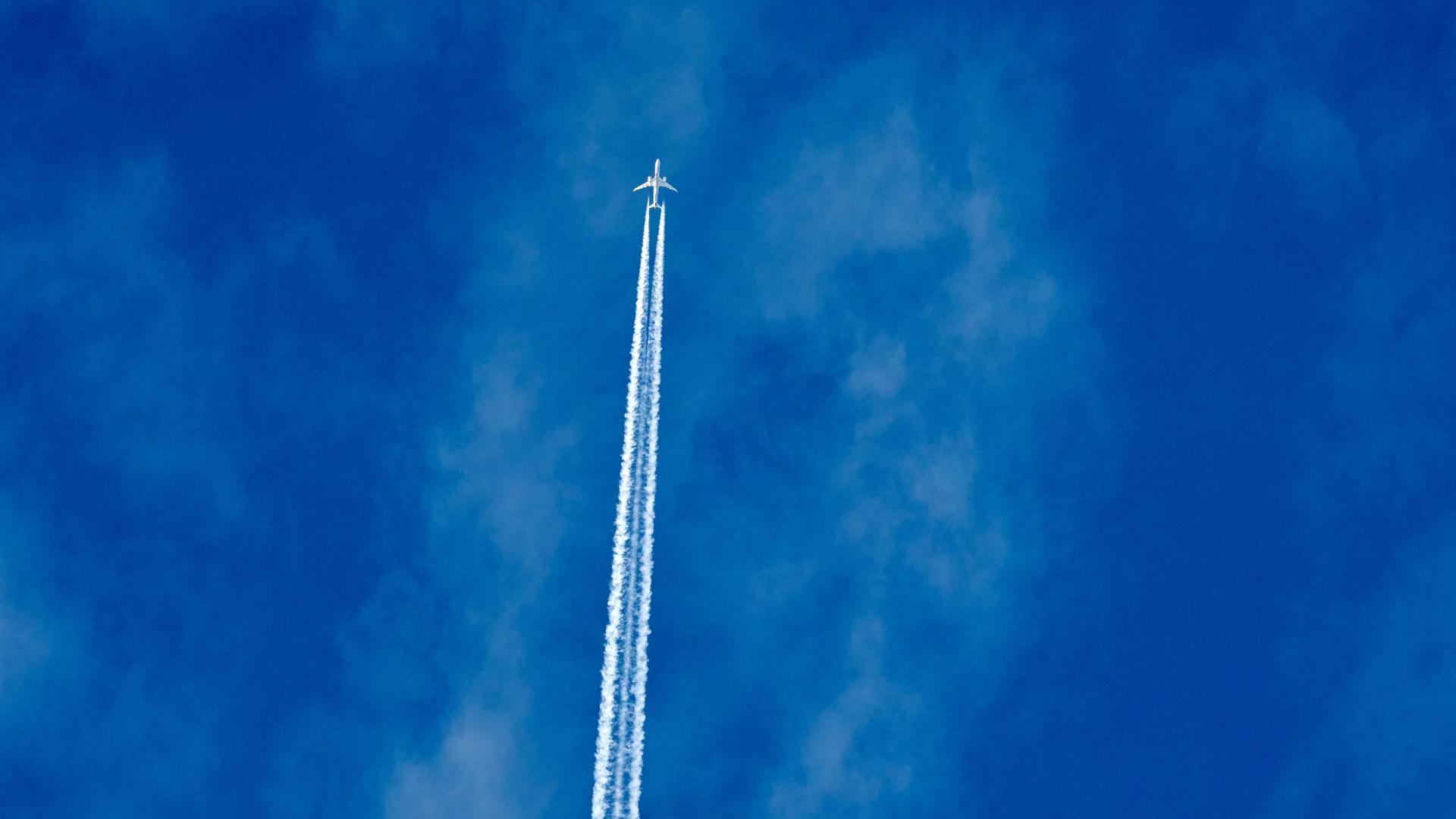 Ein Flugzeug zieht über den Himmel. Hinter ihm sind Kondensstreifen zu sehen.